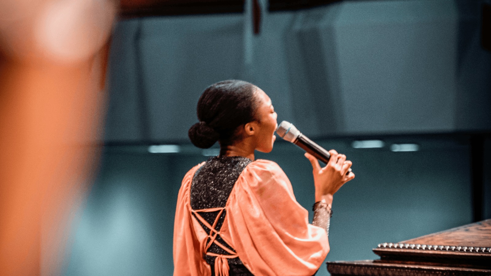 A worship leader singing into a microphone, a raised hand in the foreground